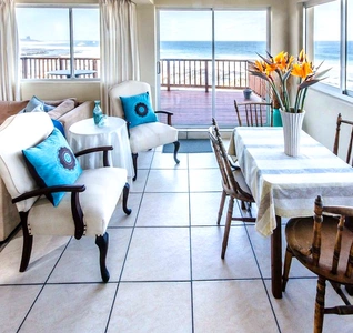 A stylish living room with a dining table, chairs, a couch, and a panoramic view of the ocean beyond the windows. A stylish living room with a dining table, chairs, a couch, and a panoramic view of the ocean beyond the windows.